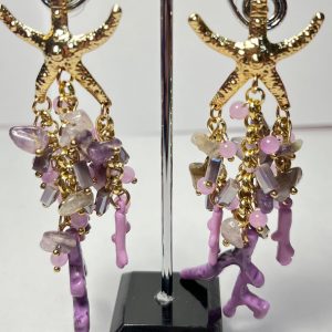 Pendientes dorados con diseño de estrella de mar y detalles colgantes en tonos morados y rosados. Elaborados con piezas de cristal, piedras naturales y dijes en forma de coral, perfectos para un look elegante y veraniego.