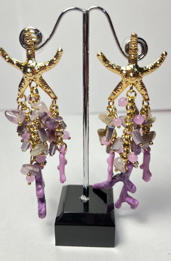 Pendientes dorados con diseño de estrella de mar y detalles colgantes en tonos morados y rosados. Elaborados con piezas de cristal, piedras naturales y dijes en forma de coral, perfectos para un look elegante y veraniego.